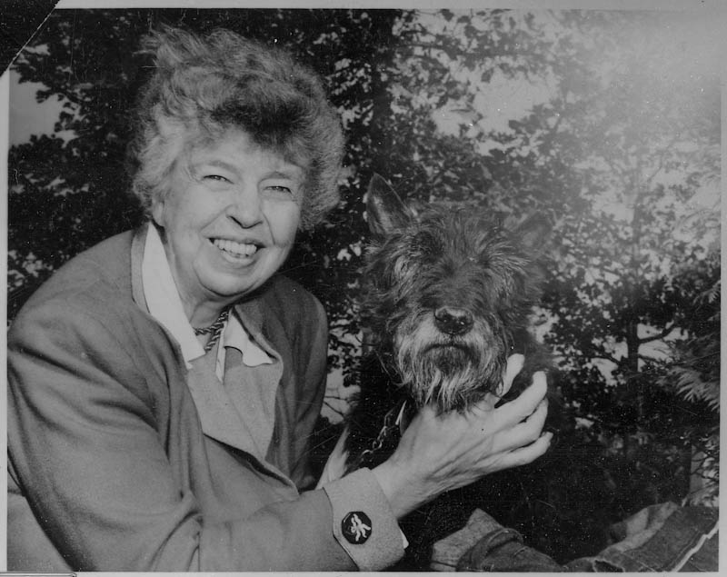 Black-and-white photo of woman sitting next to Scottie dog