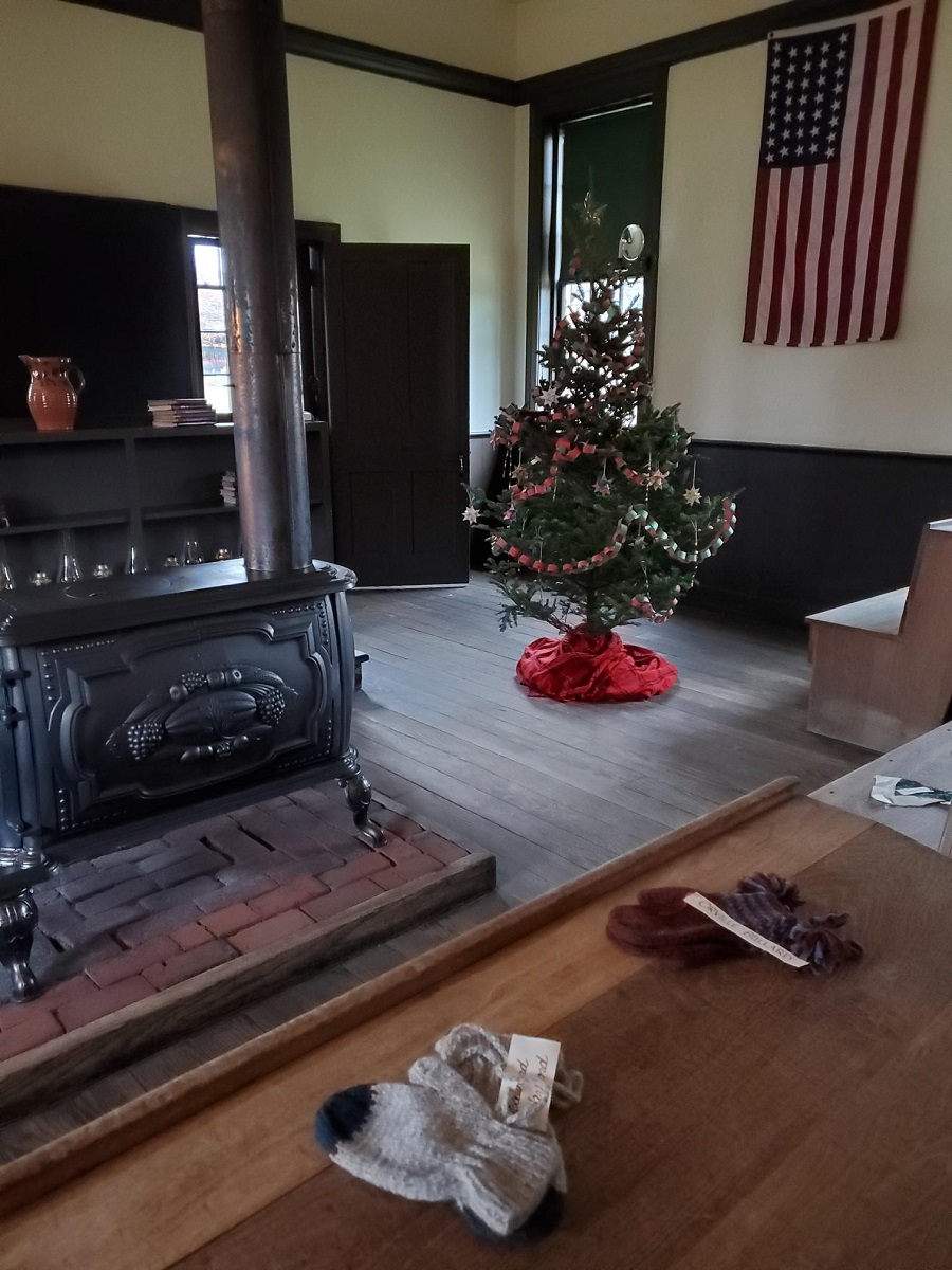 Room interior containing Christmas tree, wood-burning stove, bookshelves, and American flag hanging from wall
