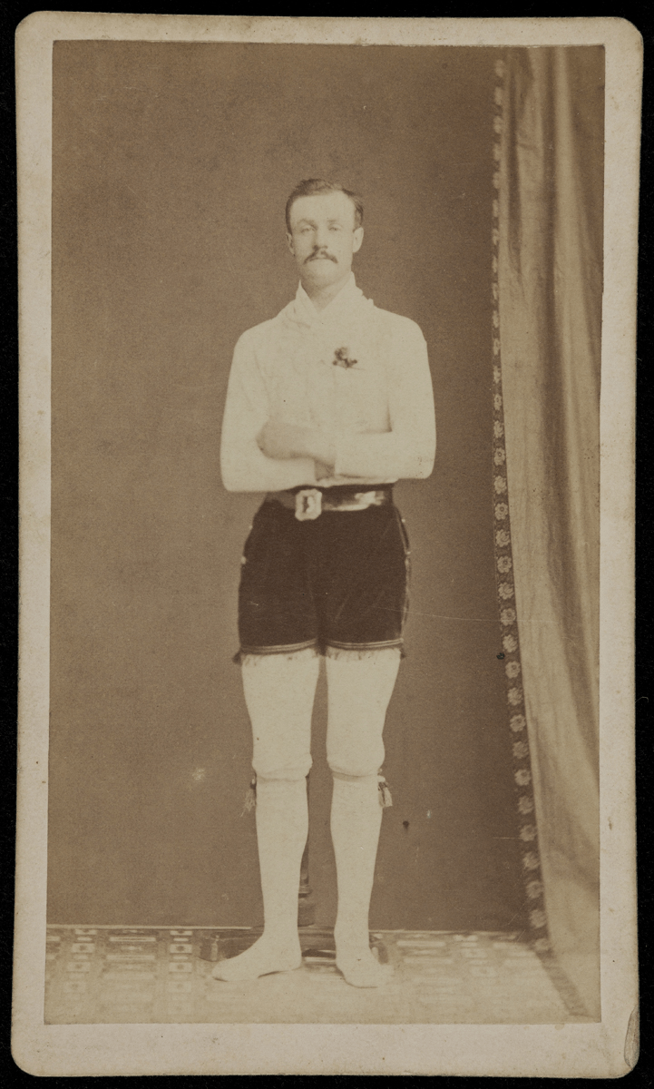 GIF cyling through four black-and-white photos of men standing with arms crossed, wearing white long-sleeved shirt, white tights (?), and dark velvet shorts with fringe