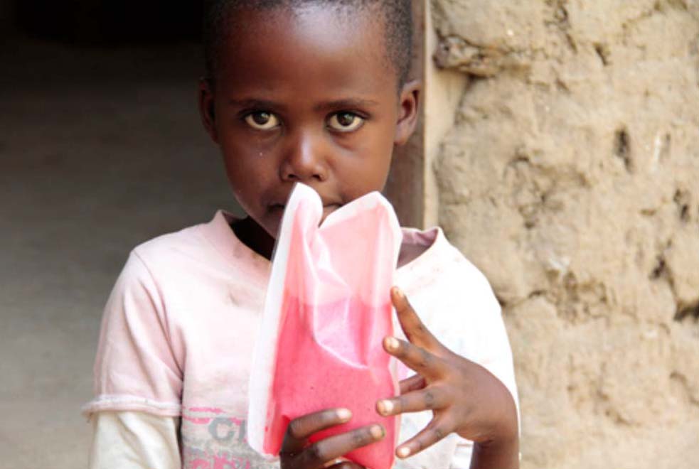 Hydropack Dark-skinned child in t-shirt holds a packet containing pink liquid to mouth