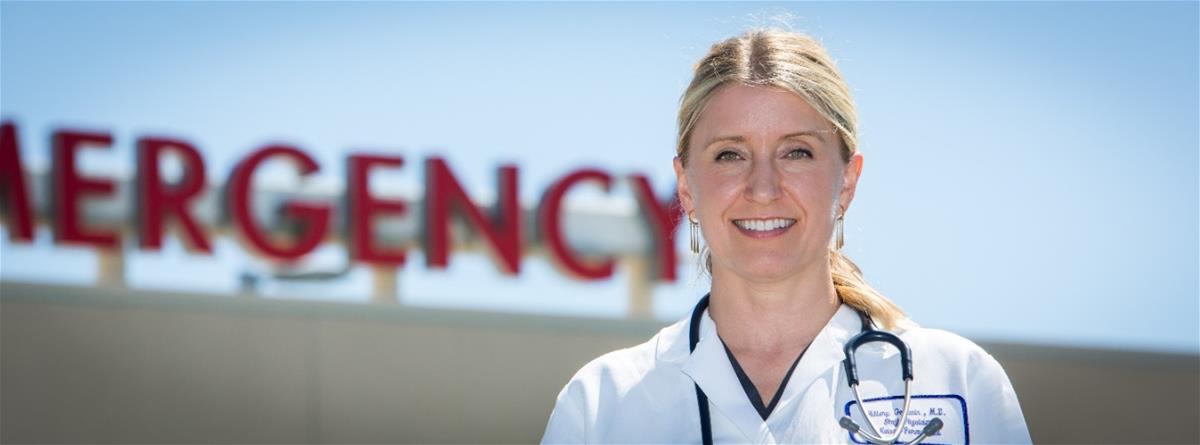 Hillary Goodwin, Auburn, California Light-skinned blonde woman in medical coat with stethoscope around neck stands in front of sign reading