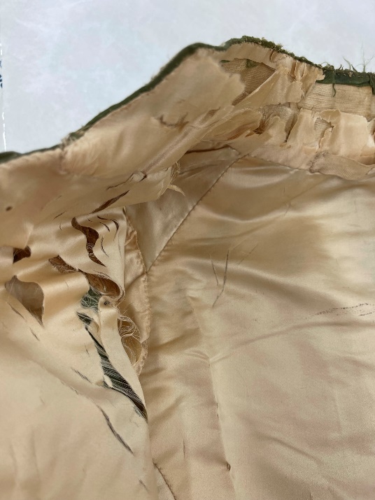 Shattered silk at the right shoulder and collar Detail of beige silk coat lining with many rips and frayed edges