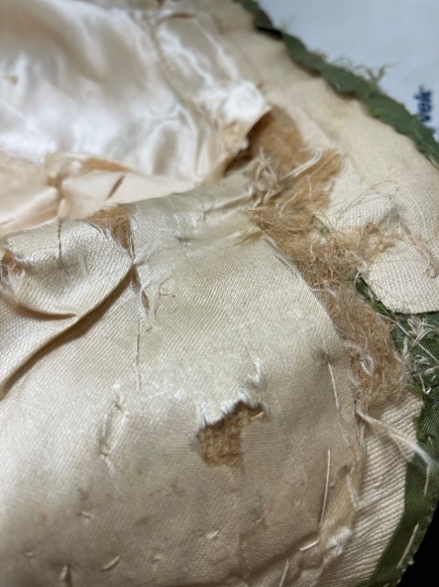 Left shoulder linen tow shoulder pad covered with the original silk Fabric fraying, stitched together but with gaps revealing stuffing underneath