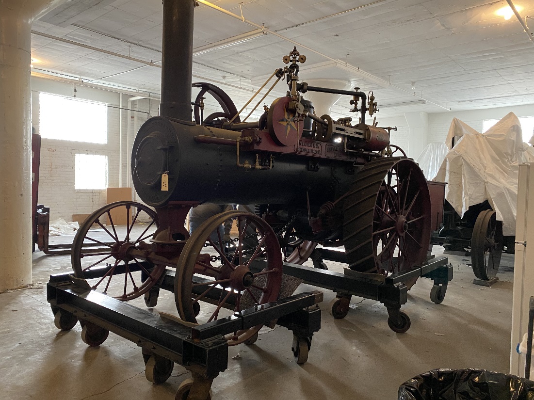A large piece of wheeled, black machinery sits on multiple dollies in a bright room
