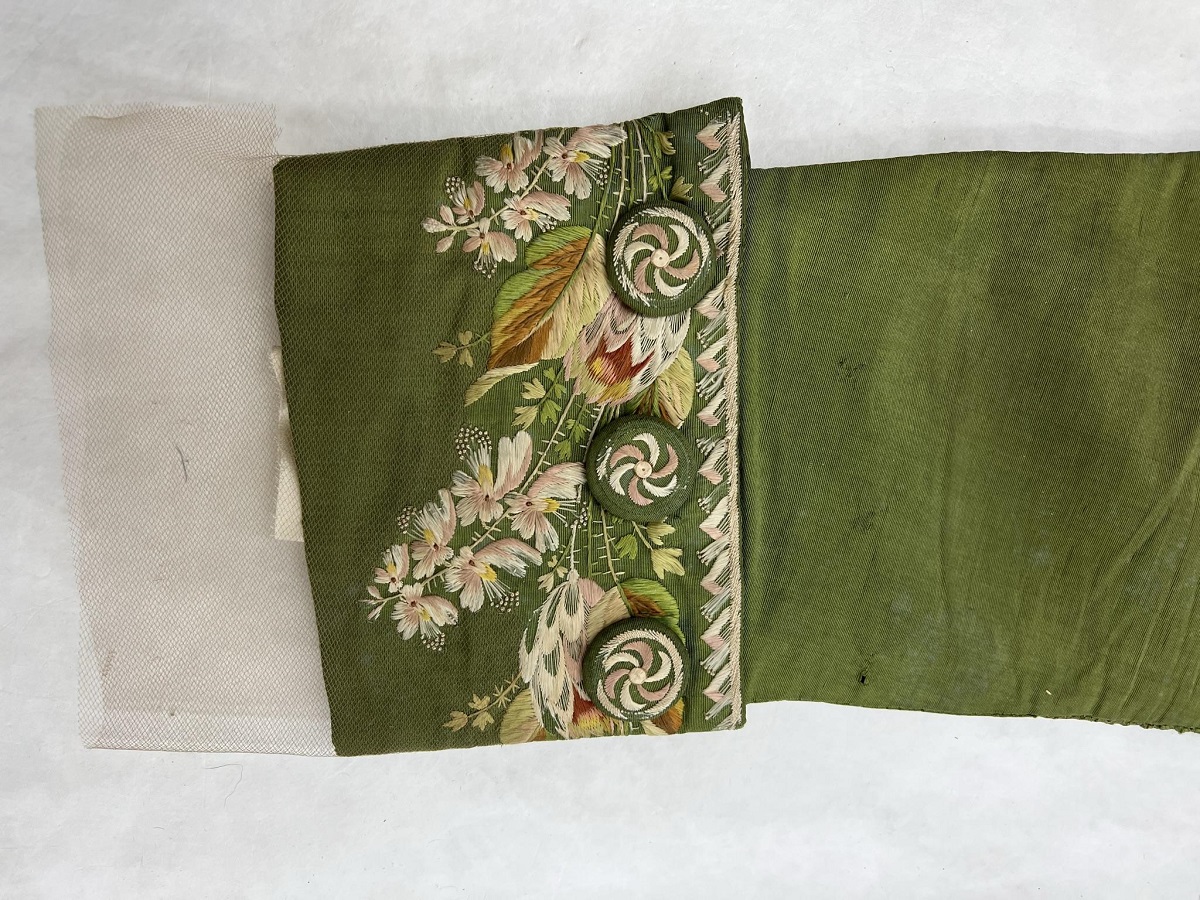 Covering the sleeves with tulle (in progress) Detail of moss-green coat sleeve with detailed floral embroidery on cuff; tulle extends from end of cuff