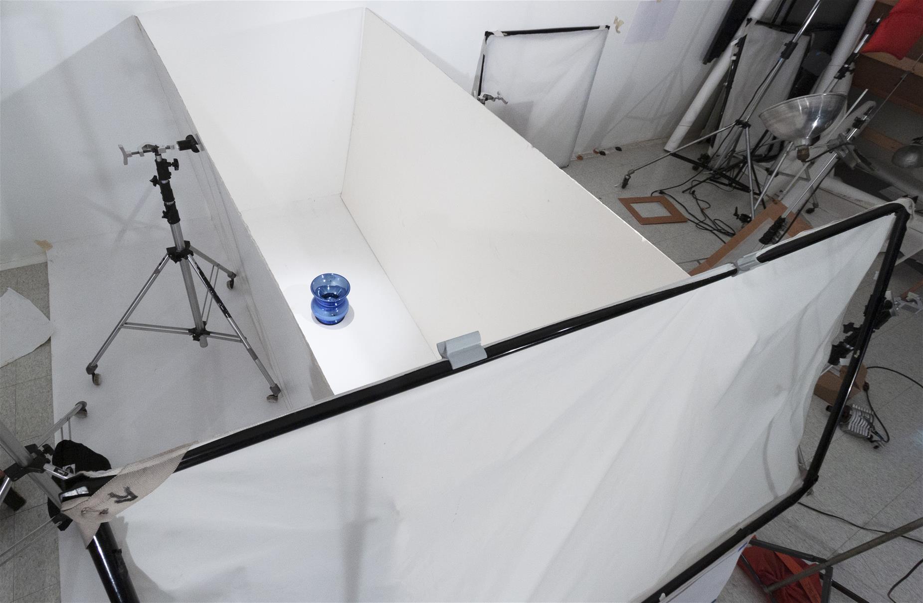 Photo Studio set up to photograph a glass spittoon Aerial shot of space blocked off with white boards and paper; blue spittoon inside space; photography equipment outside