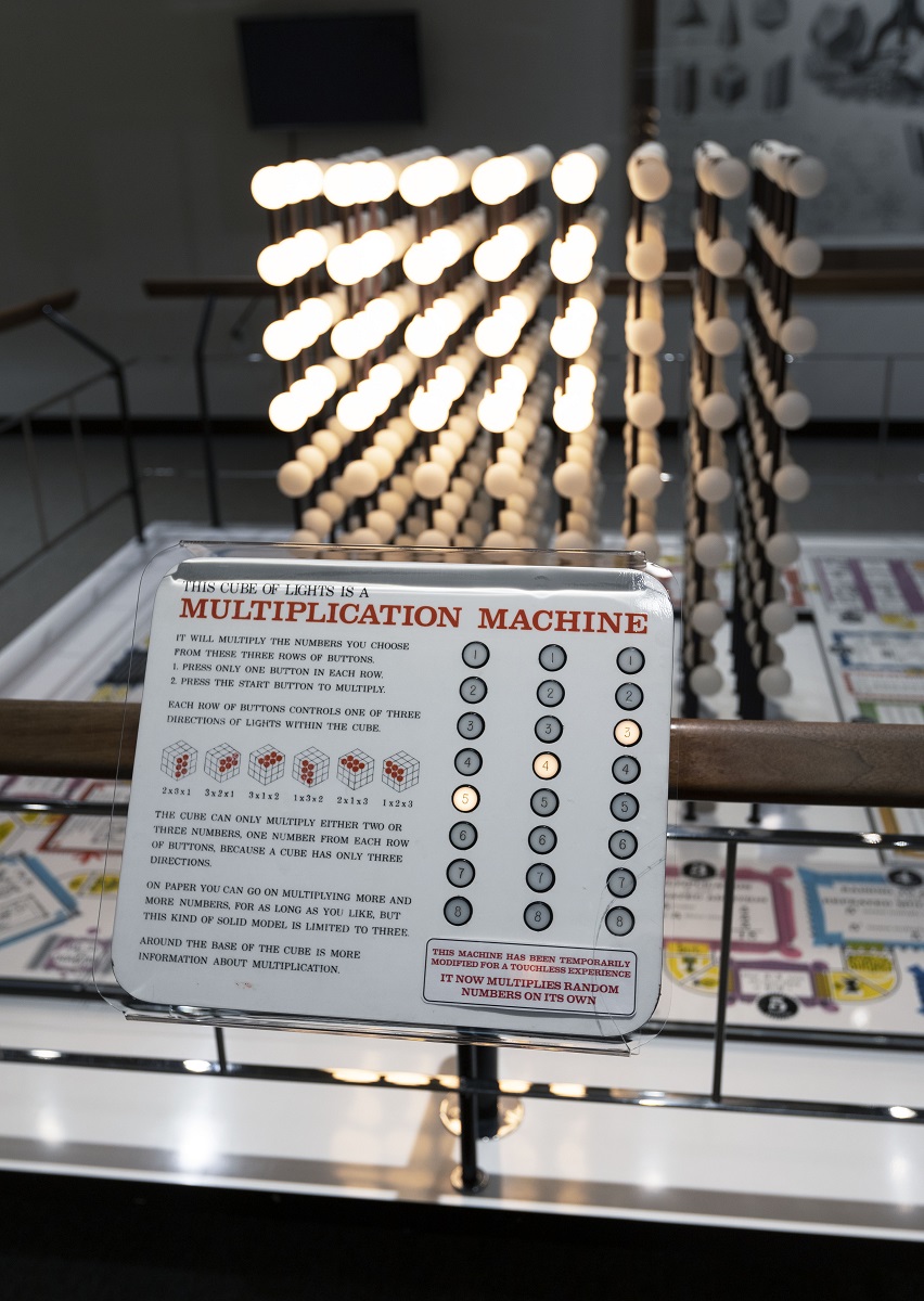 The Multiplication Machine in Mathematica was modified to run automatically during 2020 Lightbulbs arranged in a cube shape, some lit and some not, behind a wood and metal railing with a large sign in the foreground containing text