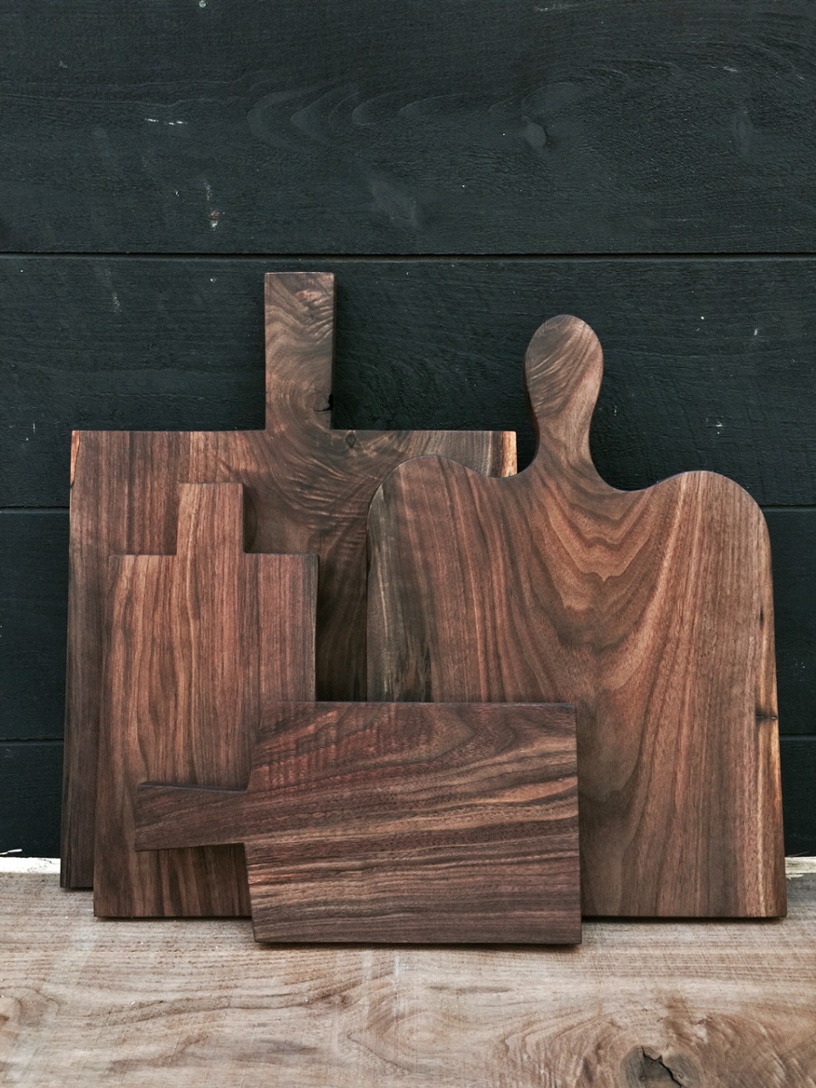 Four wooden cutting boards of different sizes, leaning against a dark gray wooden wall