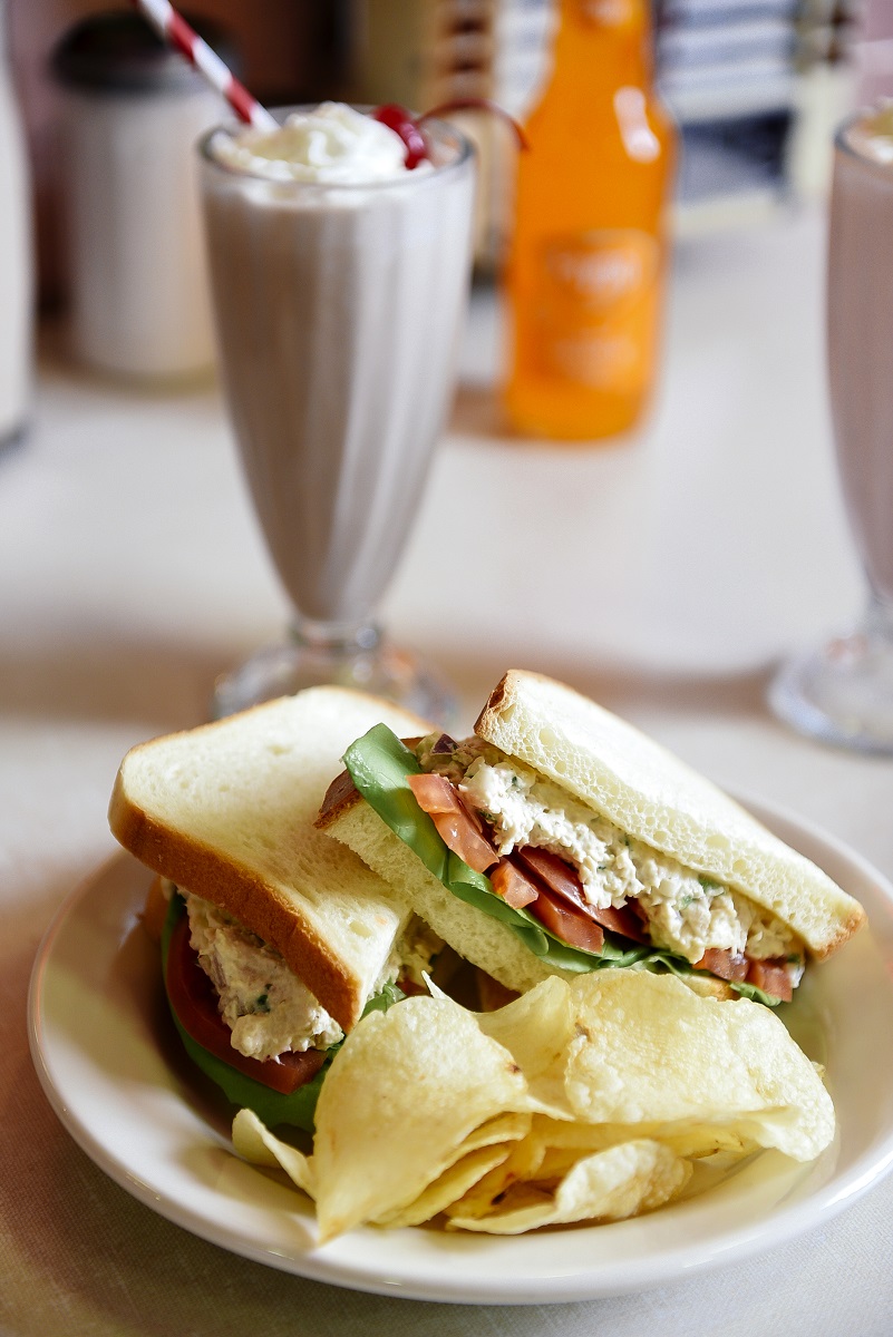 Lunch at Lamy's Plate with sandwich and potato chips sits on a counter along with a milkshake, orange Faygo in a bottle, and a napkin dispenser