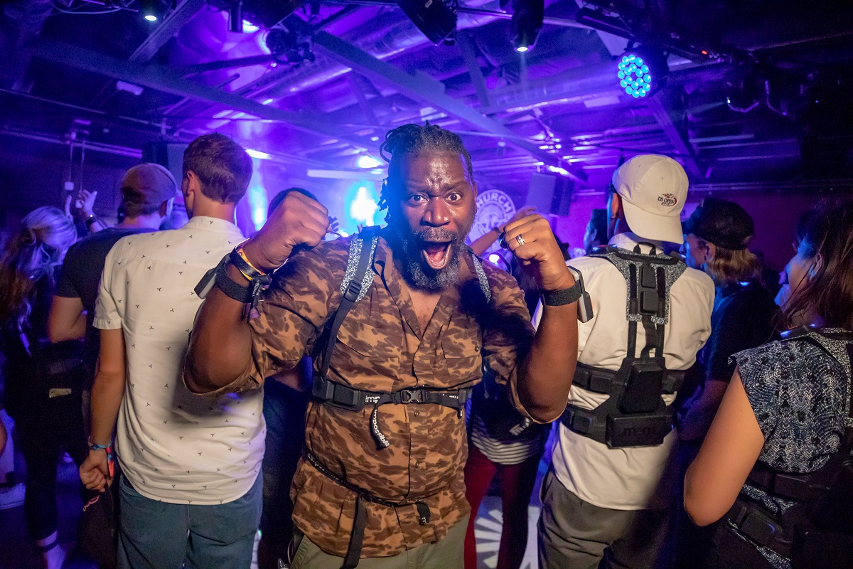 African American man faces the camera with his mouth open, while a group of people behind him face the opposite direction