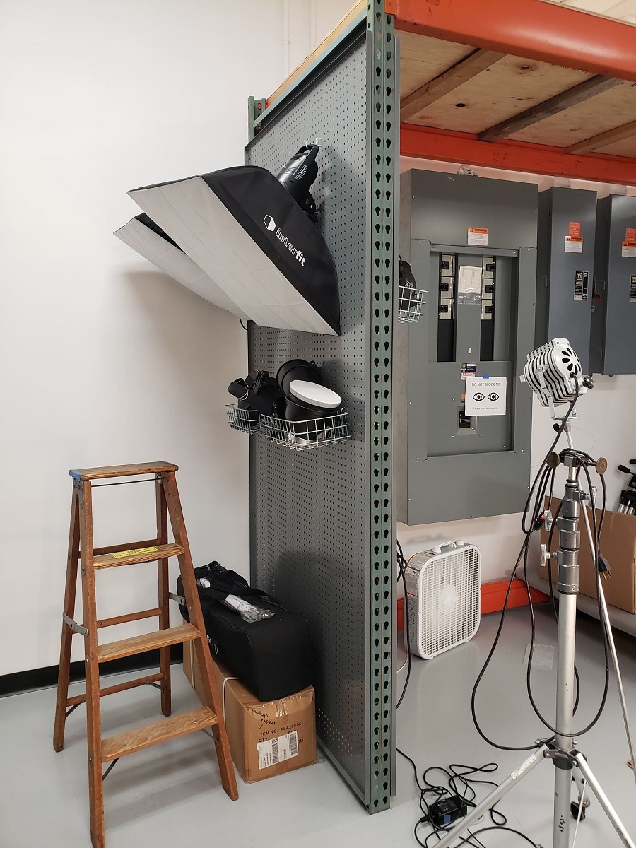 Pallet racking with lights hanging from it and a ladder on one side, and electrical boxes on the other side