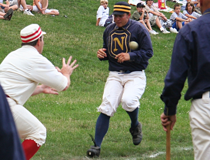 Historic Base Ball in Greenfield Village Baseball player runs toward a plate as a ball is thrown toward the baseman and spectators look on