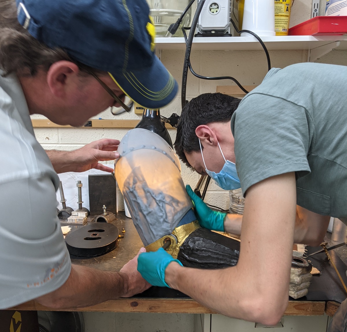The 3D-printed part is tested for fit Two people handle a hollow statuary arm on a workbench
