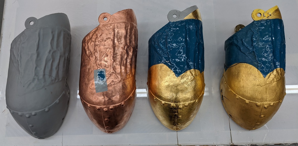 Magog's 3D-printed arm in various states Four identical tubular shapes--left one gray, next one copper, third gold and blue, right semi-dull gold and blue