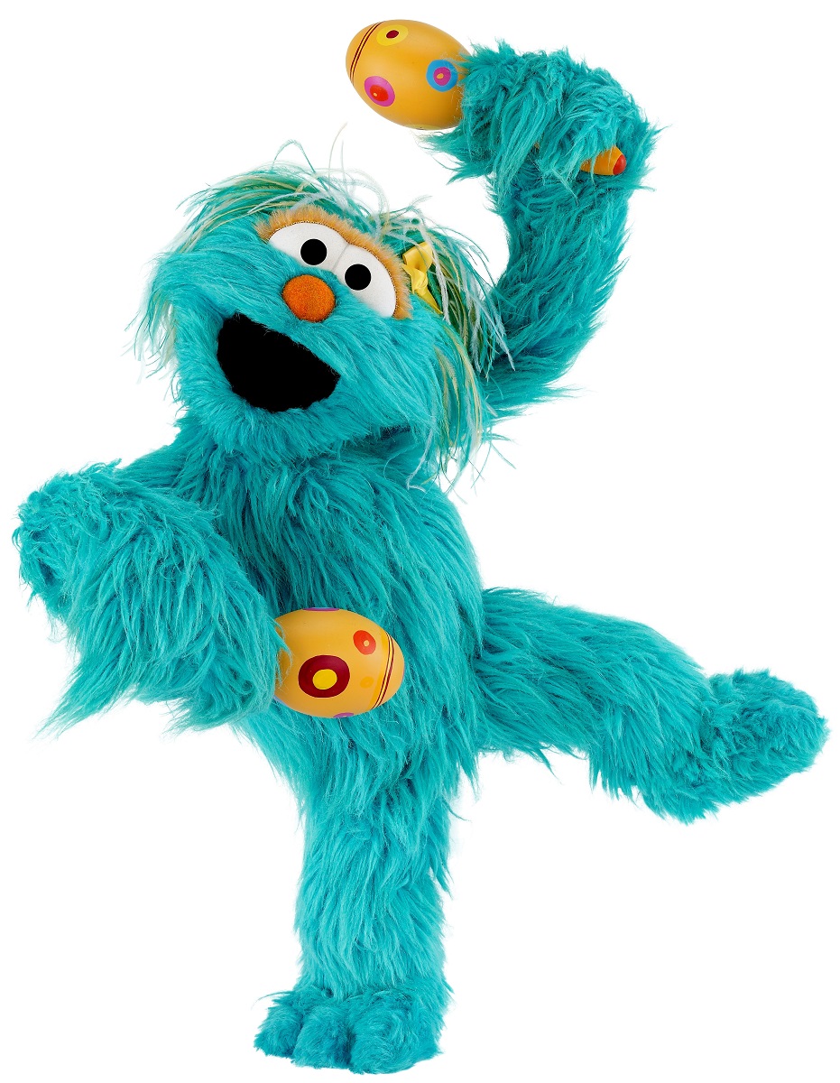 Blue furry puppet standing on one leg and holding yellow maracas