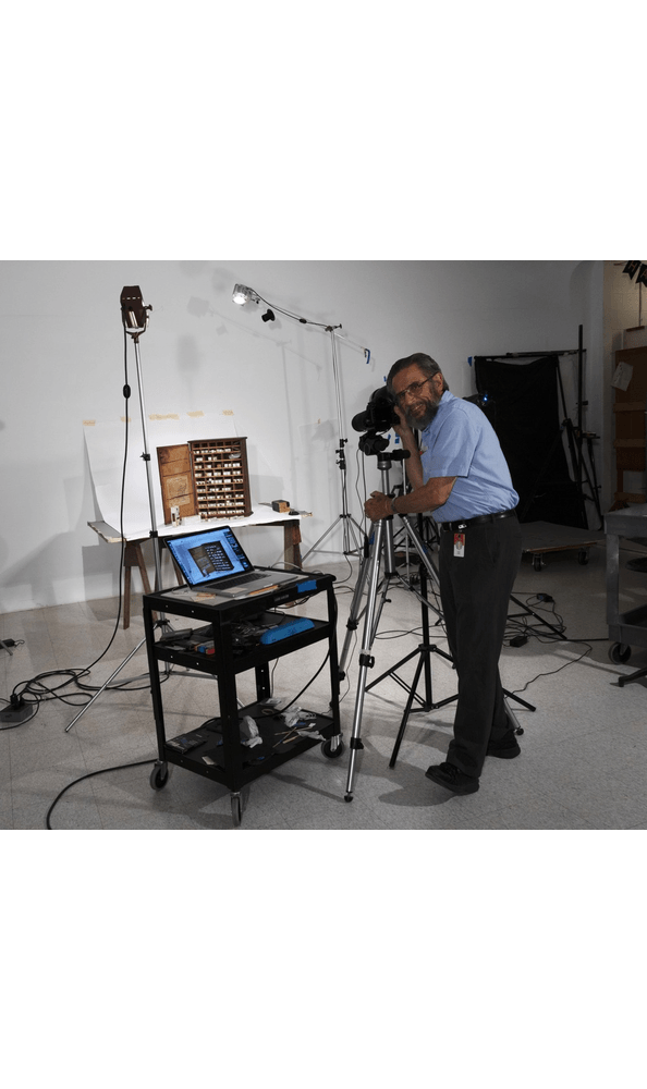 Rudy Ruzicska at work in The Henry Ford's Photo Studio, August 10, 2021 GIF cycling through a number of images of person with camera set up photographing a cabinet full of small packages
