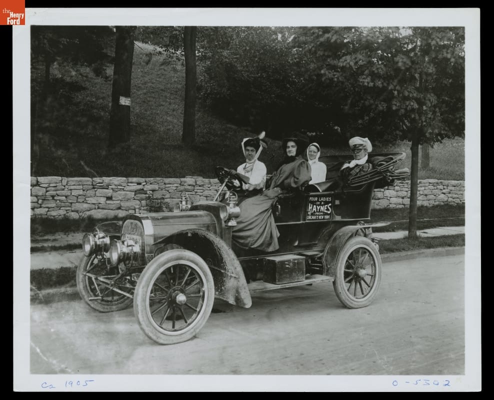 Four women in an open automobile with text on door 
