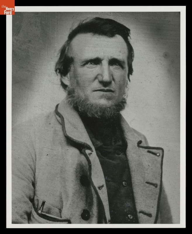 Black-and-white photo of face and torso of a man with muttonchops and beard wearing a jacket