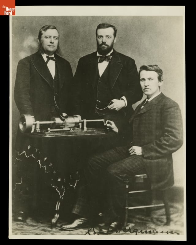 Thomas Edison, Charles Batchelor and Uriah Painter with Edison's Phonograph, April 18, 1878 Three men in suits, two standing and one seated, around a piece of equipment