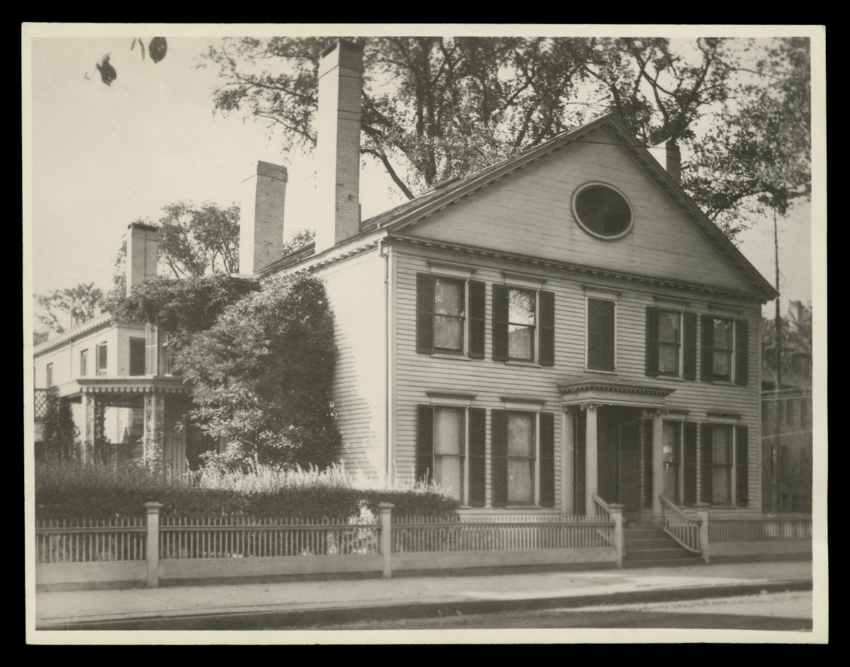 Large house, slightly overgrown/run down, with picket fence in front