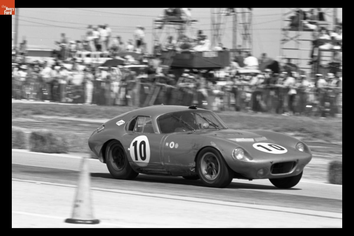 Shelby Cobra Daytona Coupe at 12 Hours of Sebring Race, March 1964 Black-and-white photo of low racecar with long hood on a track in front of fans