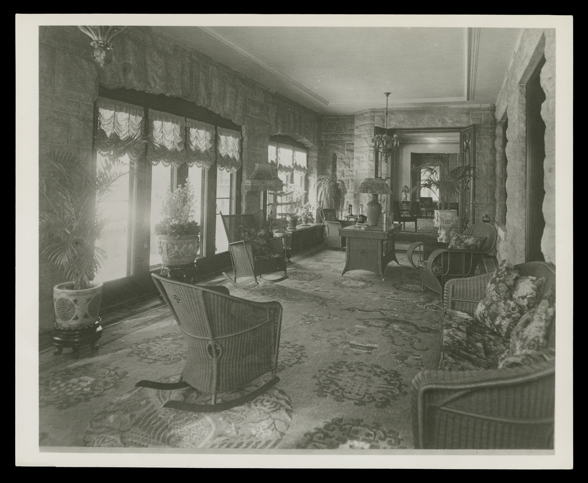 Sun Porch at Fair Lane, Home of Henry Ford, circa 1925 Black-and-white photo of long, narrow room filled with wicker furniture with many windows along one wall