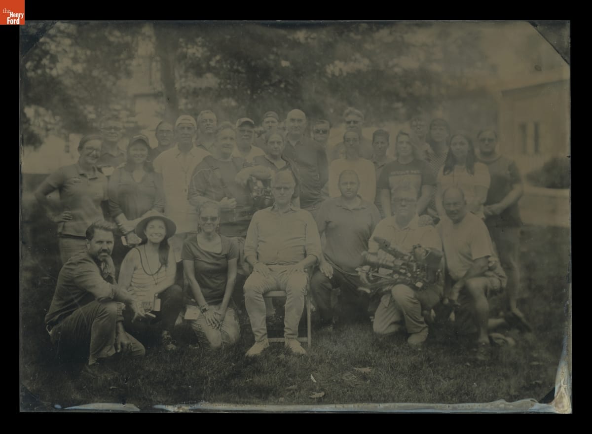 Hard-to-see black-and-white image of a group of people posed for the photo on a lawn among trees