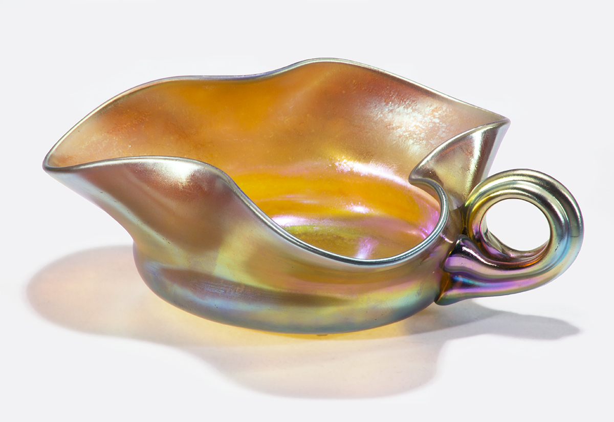 Iridescent glass leaf-shaped dish in with curved handle; amber in color