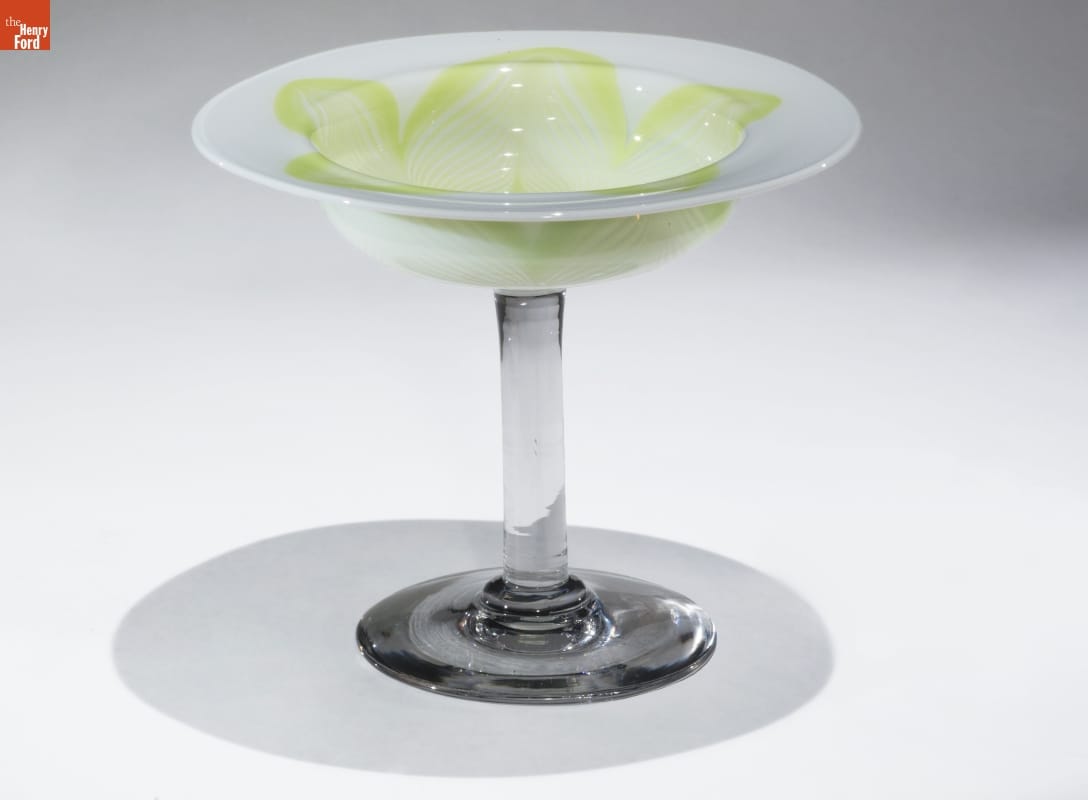 Glass dish with thick transparent glass base and stem, topped with wide, shallow white glass bowl with swirling yellow-green pattern
