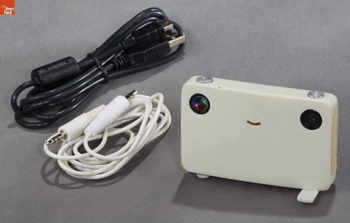 Model of White rectangular device with a smiley face and two cords, one white and one black