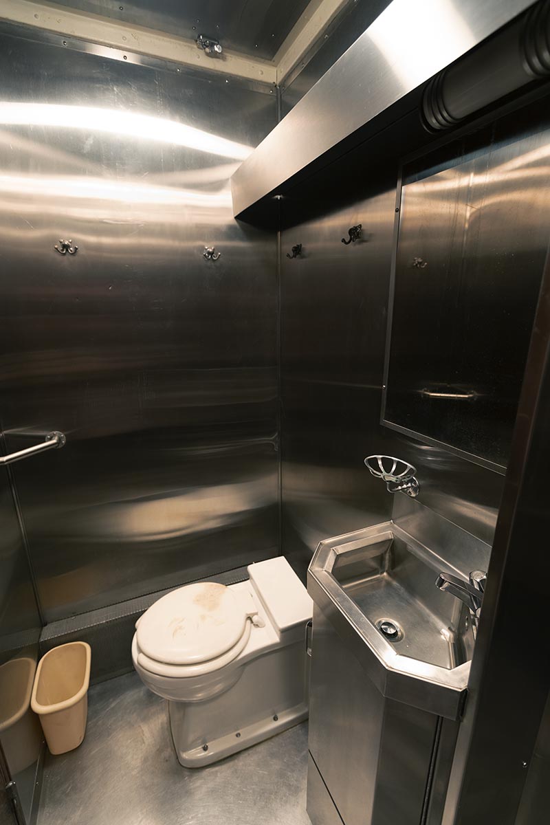 Small, stainless steel restroom containing a toilet, sink, and mirror