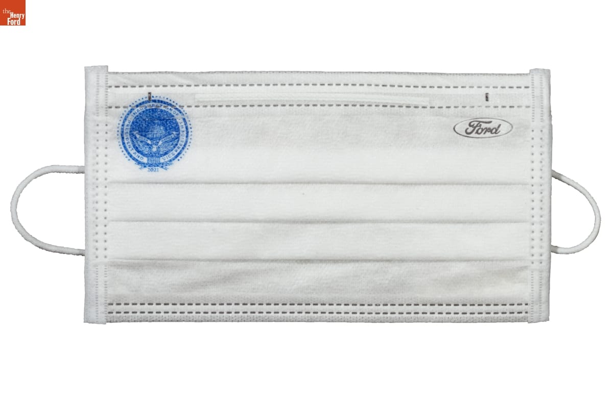 White pleated cloth or paper face mask with Ford logo in upper right and blue circular logo in upper left 