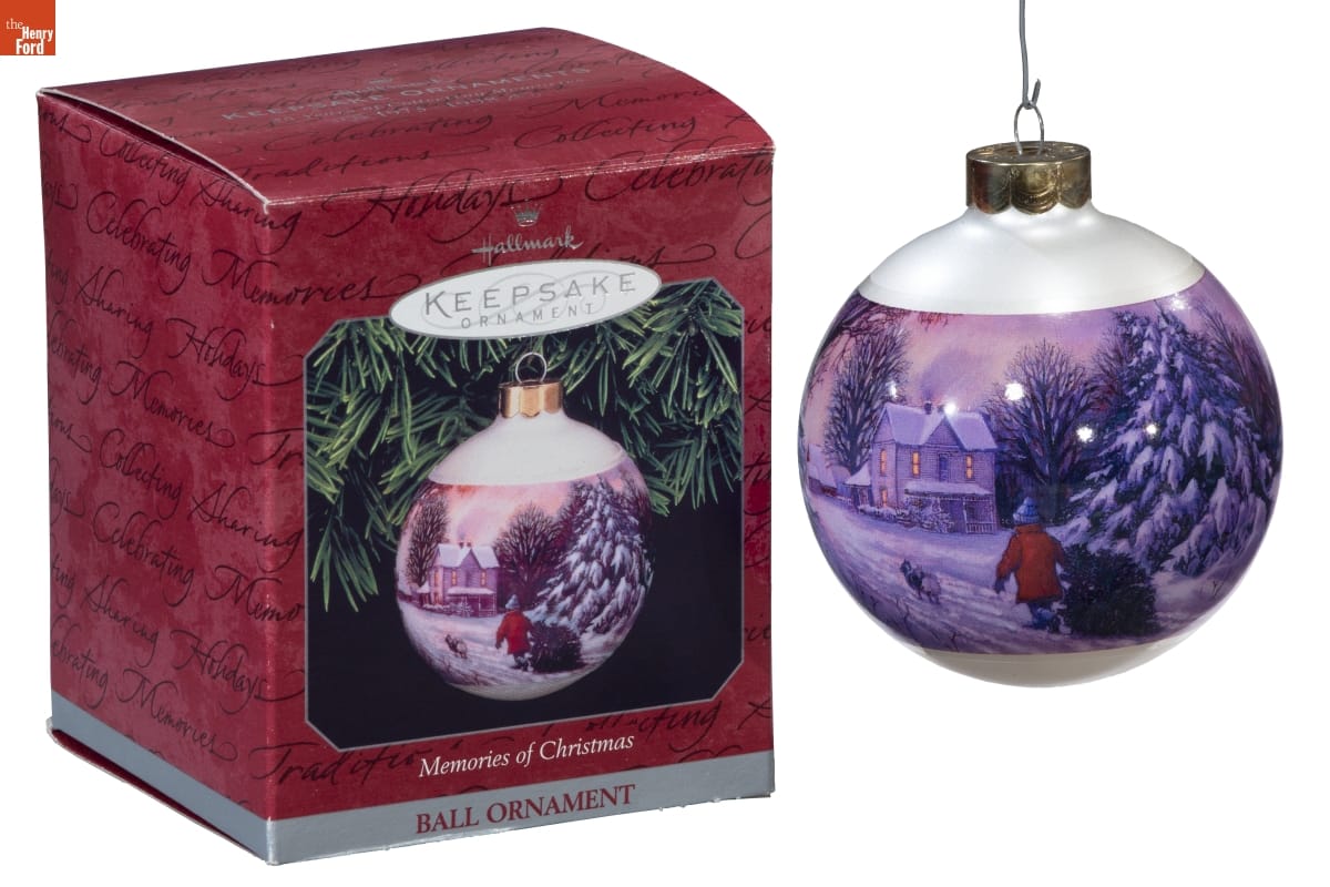 Hallmark White bulb ornament with image of person dragging Christmas tree across a snowy field toward a house; box for ornament is also in photo