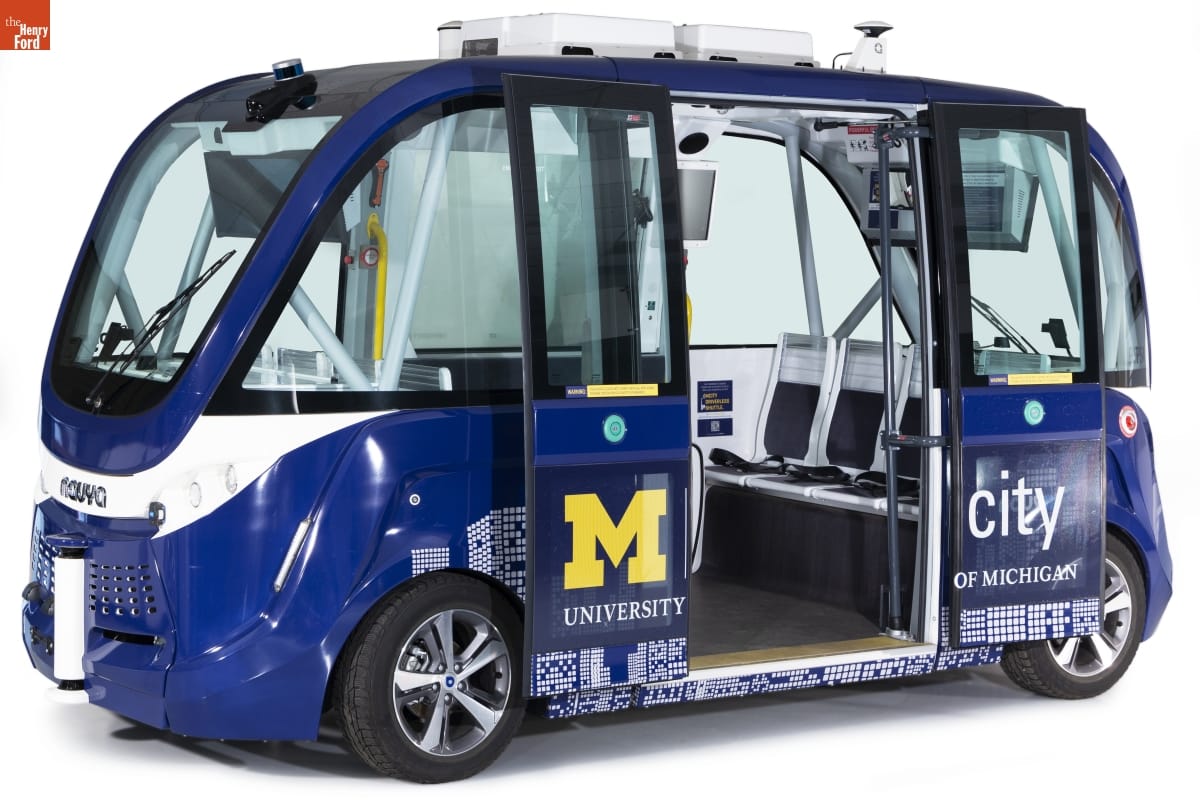 Squat blue van with large glass windows all the way around and doors slid open; text and graphics on side 