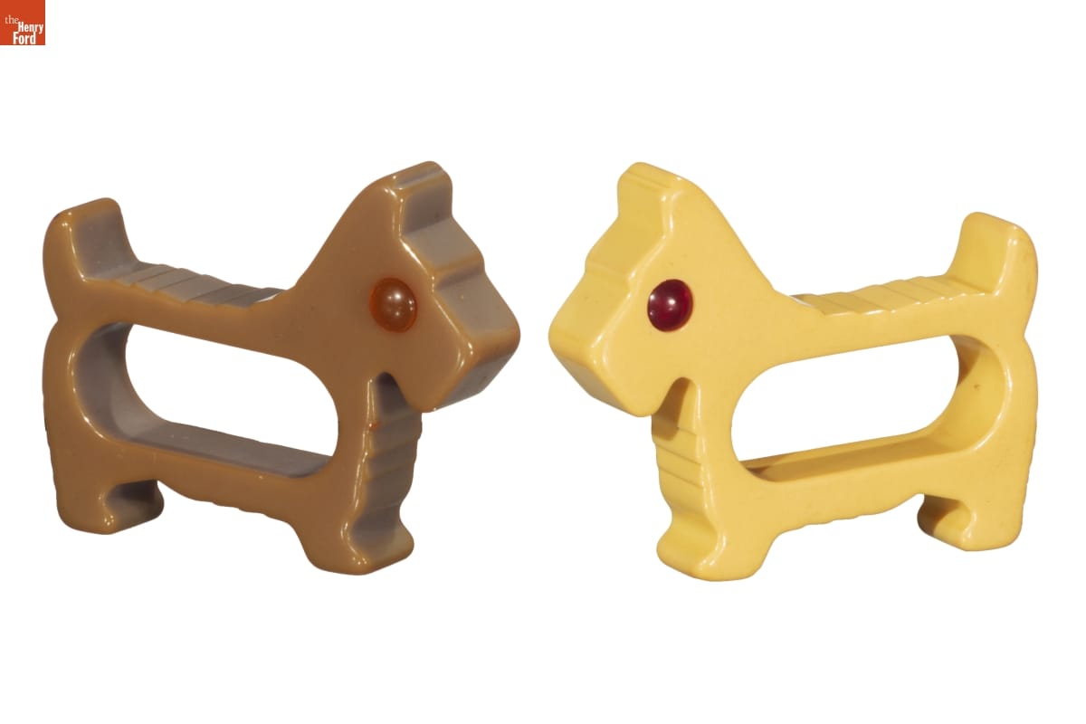 Two napkin rings, one beige and one brown, in the shape of Scottie dogs with red eyes
