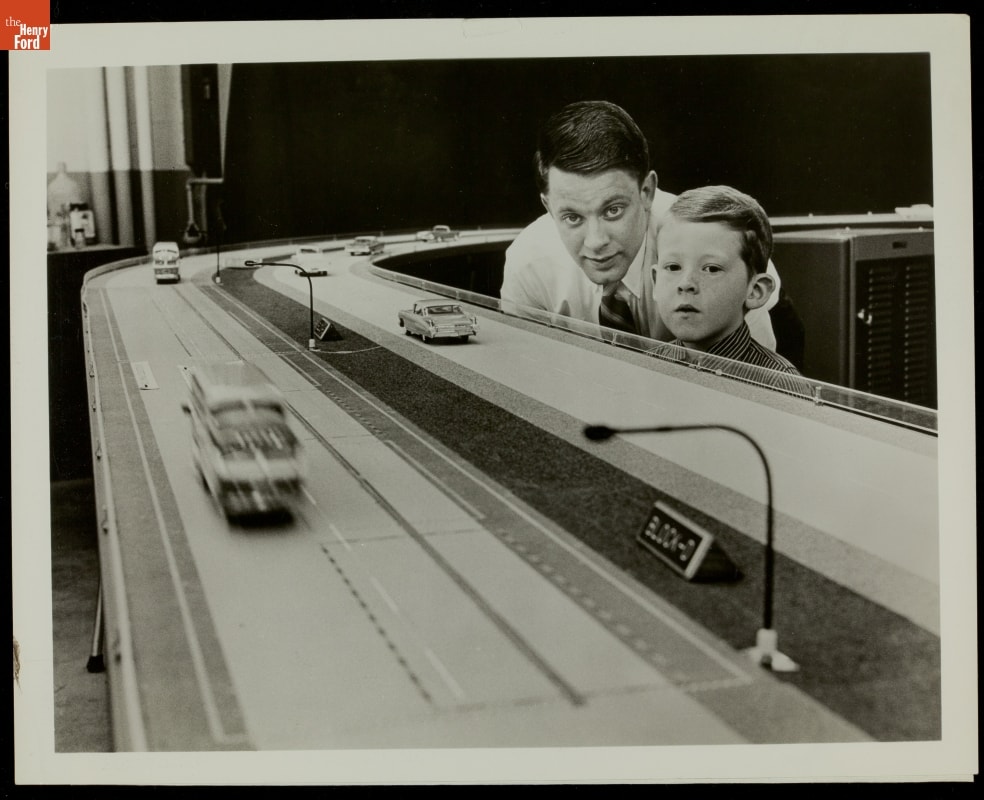 Young boy and young man look at eye level at a large model of a road with cars
