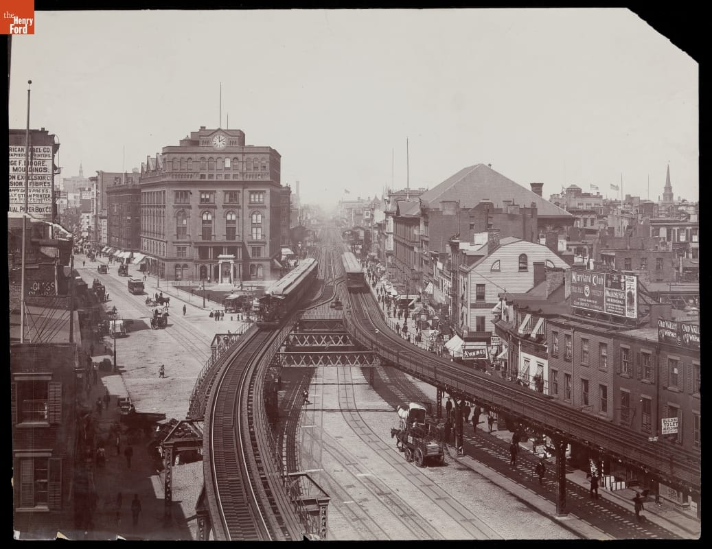 Aerial, black-and-white photo of elevated train tracks, roads, and buildings