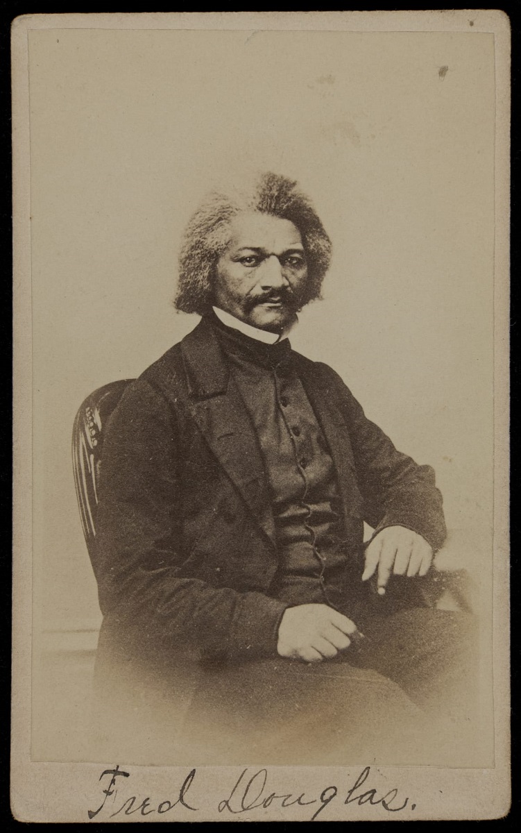 Man with mustache and bushy hair sits in chair and looks at camera