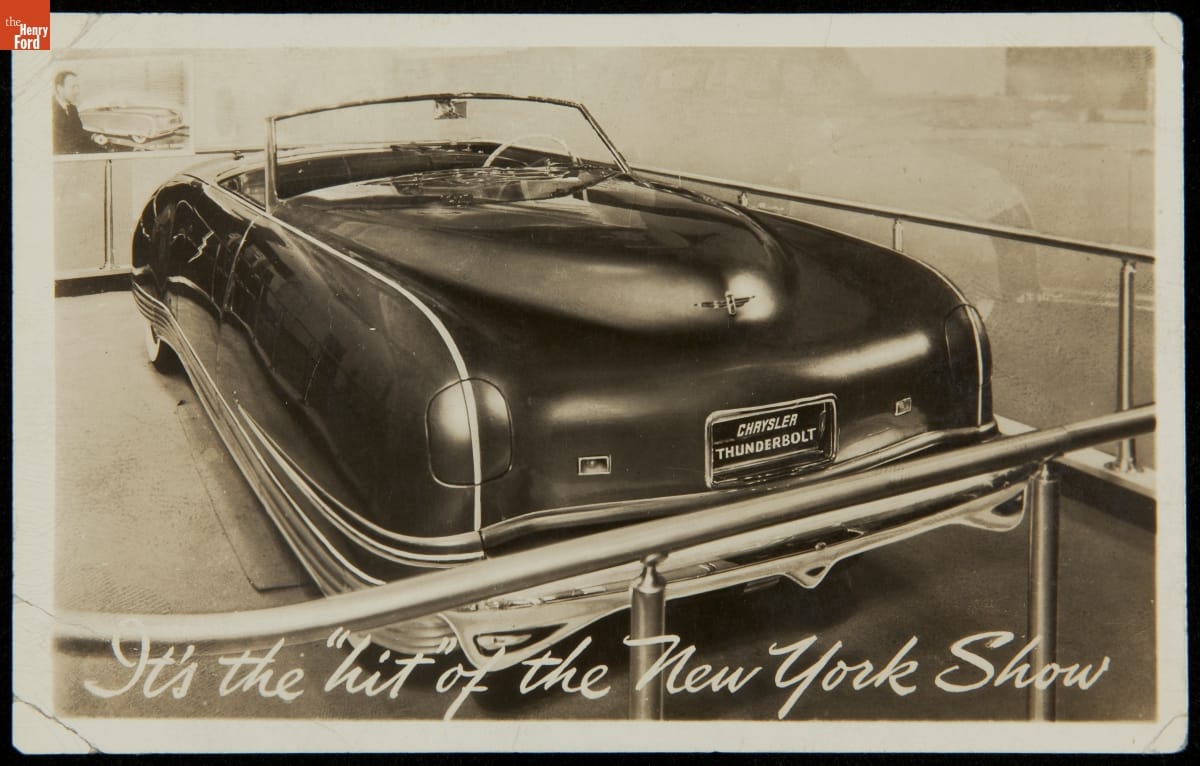 Long, rounded car surrounded by barriers; contains text