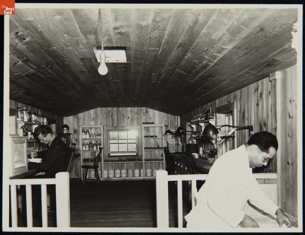 Worker Making Soybean Bread inside the Soybean Laboratory in Greenfield Village, Dearborn, Michigan, circa 1935 Room with work surfaces along walls filled with equipment; two men work in the space