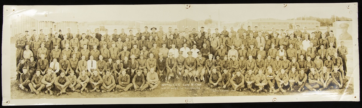 Panoramic photograph of large group of people, posed sitting and standing, many in uniform