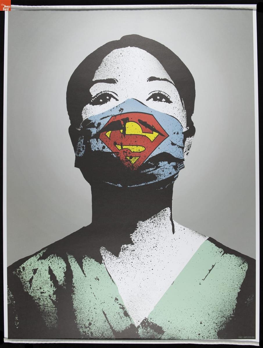 Portrait of woman with dark hair in green scrubs wearing blue face mask marked with yellow and red 