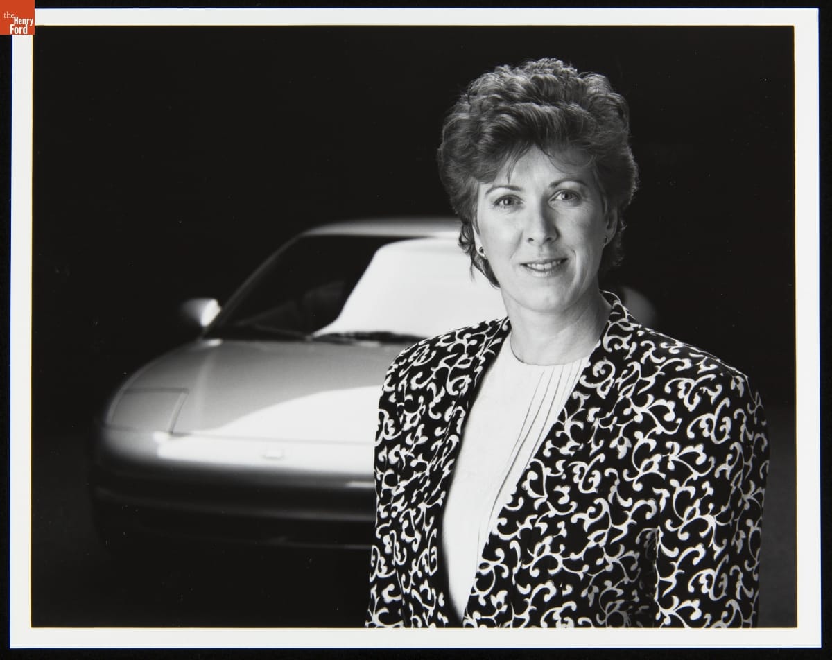 Portrait of Mimi Vandermolen, 1992-1993 Woman with short hair wearing a jacket with a stylized vine pattern poses in front of a car