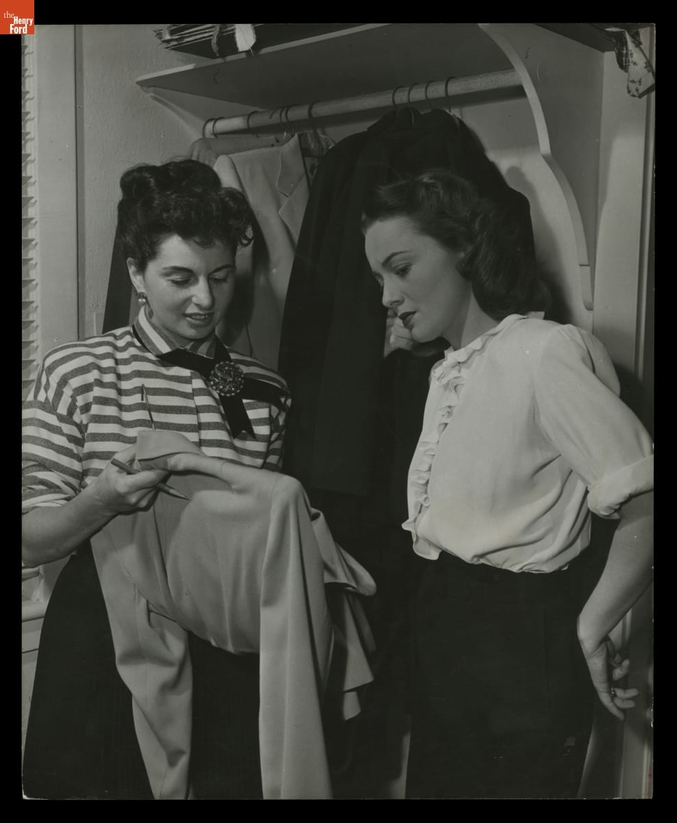 Studio Image of Designer Bonnie Cashin with Actress Olivia de Havilland, 1948 Black-and-white photo of two women standing in front of a closet with hanging clothing, looking at a blouse or jacket one of them is holding