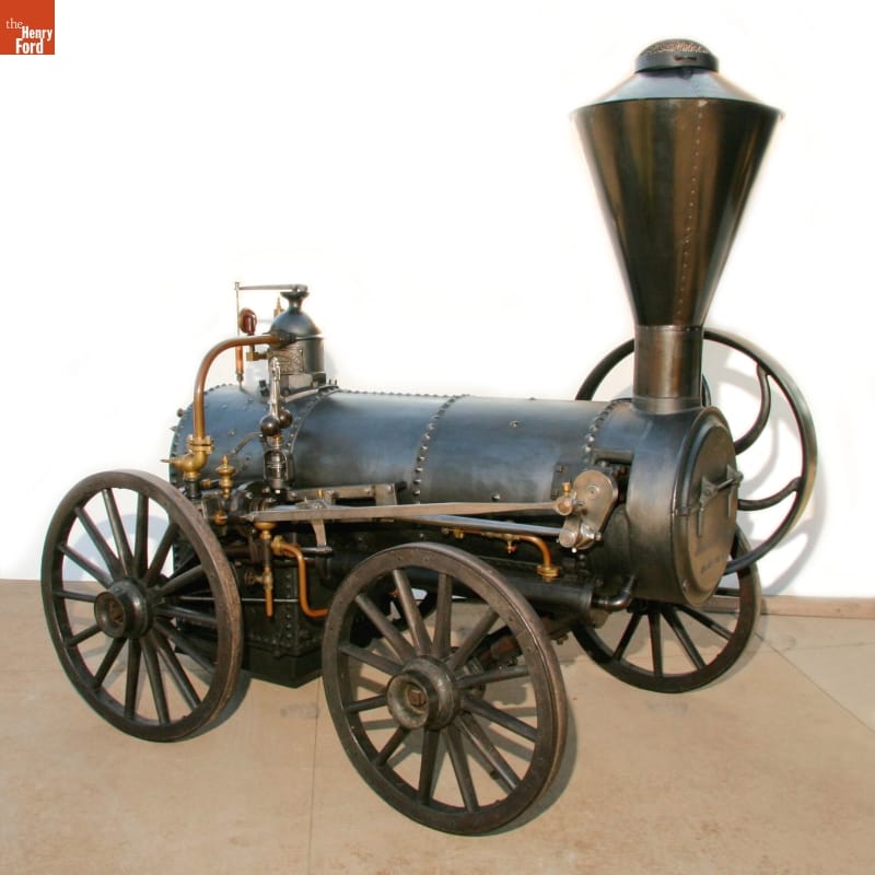 Horizontal cylindrical engine mounted on four wheels with a chimney or stovepipe at one end