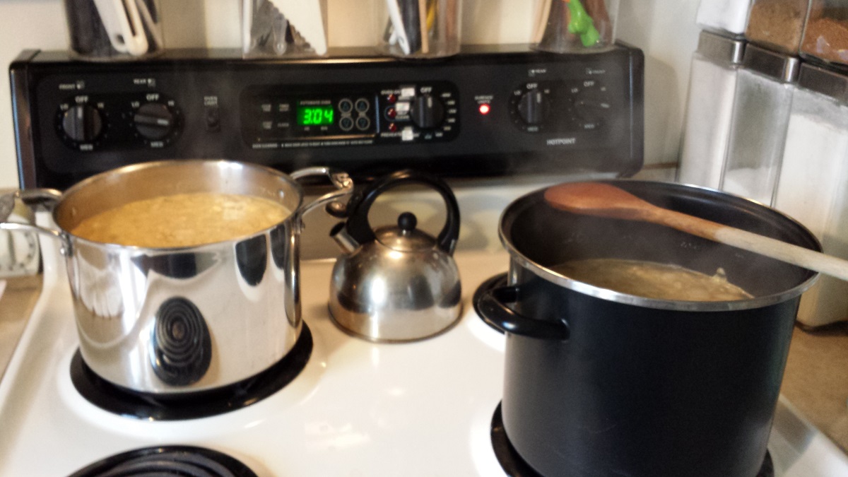 Stovetop with two steaming stockpots filled with soup